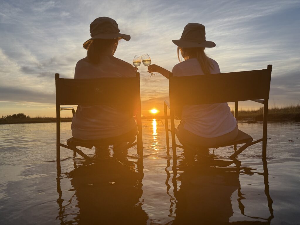 Two women toasting at sunset with international travel agent planning.